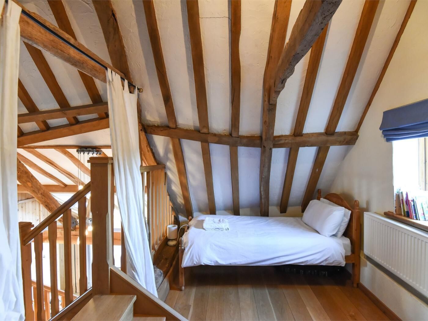 Ein Schlafzimmer mit Holzboden, einem Bett, einem Fenster und einer Treppe.