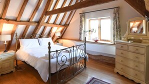 Ein Schlafzimmer mit geneigter Decke, einem Bett, einer Kommode, einem Fenster mit Vorhängen und einer Lampe.