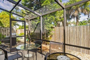 Eine verglaste Terrasse mit Tisch und Stühlen, umgeben von einem Bambuszaun und Bäumen.