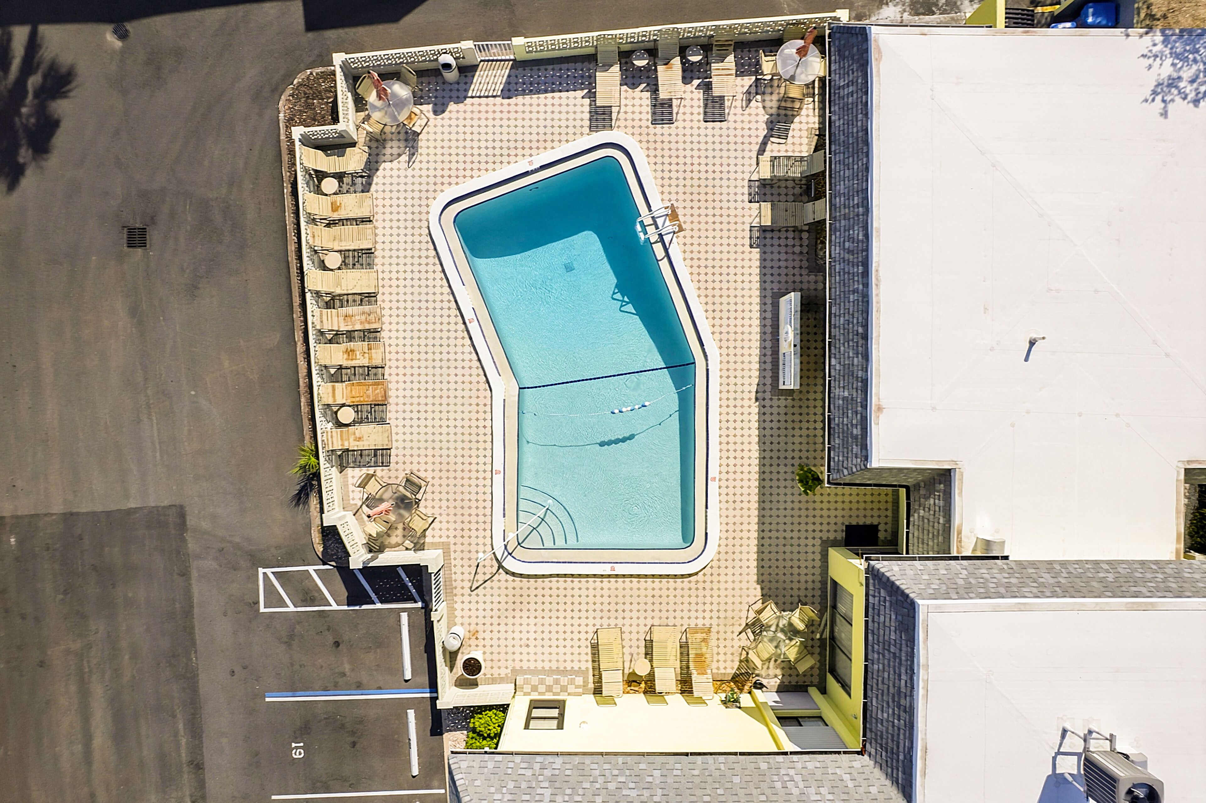 An aerial view of a swimming pool with a geometric shape, surrounded by lounge chairs and a small deck area.