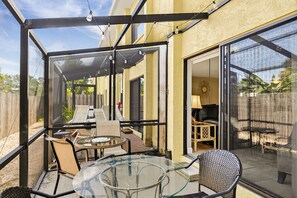 A covered patio with a glass table and chairs, a wooden fence, and a view of a backyard. - 1st floor walk to restaurants and beach (Siesta Key)