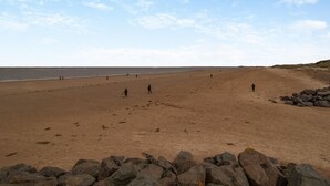 Uma extensa praia de areia com céu claro e um litoral rochoso.