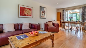 Uma sala de estar com mesa de centro de madeira, sofás de couro e uma área de jantar com mesa e cadeiras de madeira.