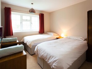 Ein Schlafzimmer mit zwei Betten, einem fensterbelaubten Fenster, einer Nachttischlampe und einer Holzbank mit Handtuch.