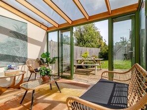 Eine sonnendurchflutete Terrasse mit Korbmöbeln, einem Glastisch und Blick auf den Garten.
