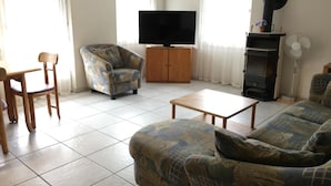 Ein Wohnzimmer mit Sofa, Sessel, Fernseher und Kamin.