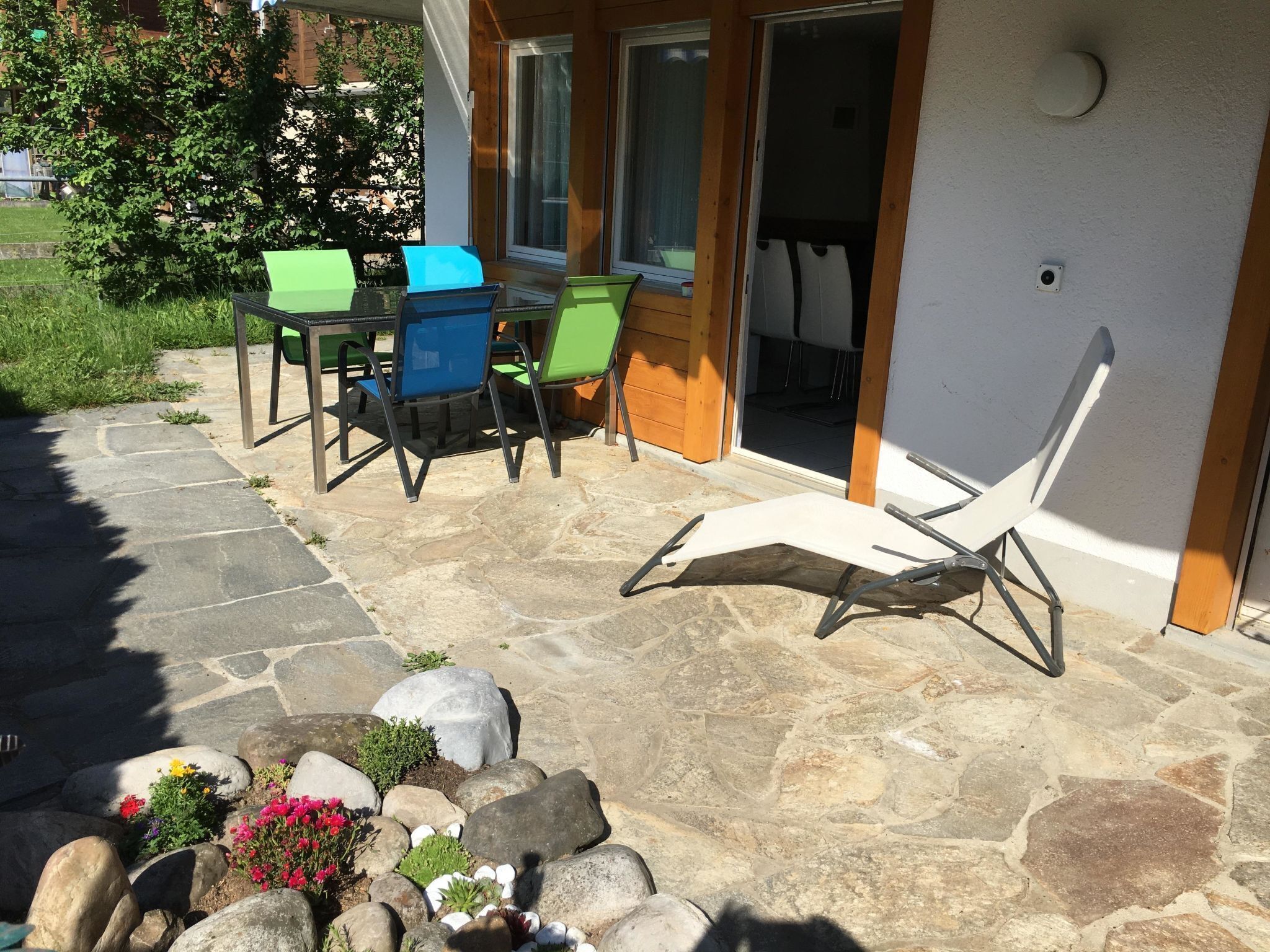 Een terras met stenen vloer, tuinmeubilair en een kleine rotstuin met bloemen.