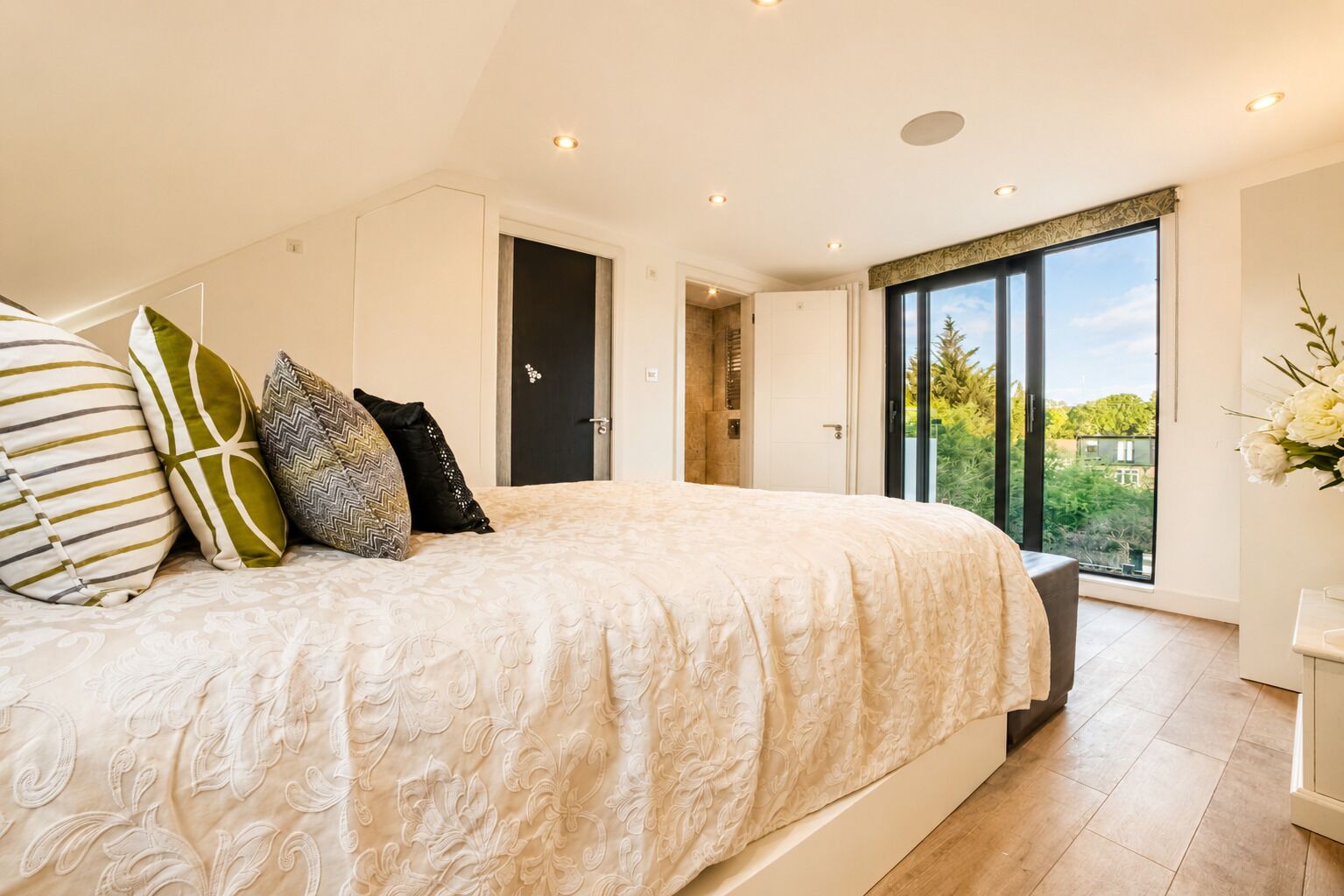 A bedroom with a large bed, multiple pillows, a wardrobe, a door, and a window with a view.
