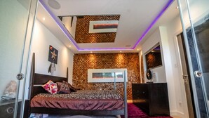 A bedroom with a bed, a desk, a wall-mounted TV, and a ceiling with a checkered pattern. - Design-Led 3-Bed Home with Garden, Sauna, Hot Tub & Parking (Greater London)