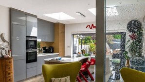 A modern kitchen with grey cabinets, a central island, and red chairs. - Design-Led 3-Bed Home with Garden, Sauna, Hot Tub & Parking (Greater London)