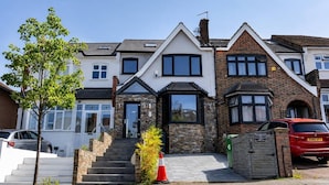 A two-story residential building with a stone facade, a central entrance with a glass door, and a visible staircase leading to the entrance. - Design-Led 3-Bed Home with Garden, Sauna, Hot Tub & Parking (Greater London)