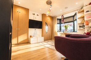 A modern living room with wooden cabinets, a flat-screen TV, a meditation statue, and a purple sofa. - Design-Led 3-Bed Home with Garden, Sauna, Hot Tub & Parking (Greater London)