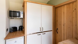 Una kitchenette con microondas, tostadora y cafetera sobre una encimera de madera, un refrigerador blanco y un armario de madera con pomo.