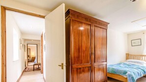 Un dormitorio con un armario de madera, una cama con una manta azul y un pasillo que conduce a otra habitación.