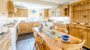 Una cocina amplia con armarios de madera, una mesa de comedor para cuatro personas y un gran ventanal que proporciona luz natural.
