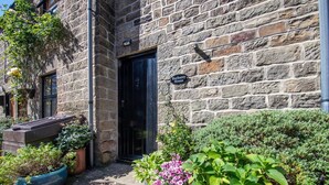 Un edificio de piedra con una puerta negra, un letrero que dice 'Buchanty House' y plantas en macetas al frente.