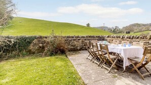 Un muro de piedra con una mesa lista para comer, con vista a una colina verde.