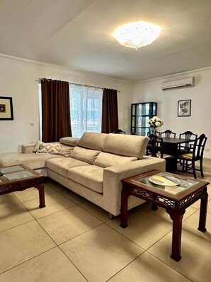 A living room with a sofa, a glass coffee table, a dining table with chairs, and a chandelier. - Fort Cambridge - Sliema - Malta (Sliema)
