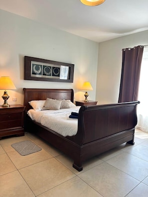 A neatly made bed with white linens, two bedside tables with lamps, a framed artwork above the bed, and a window with curtains. - Fort Cambridge - Sliema - Malta (Sliema)
