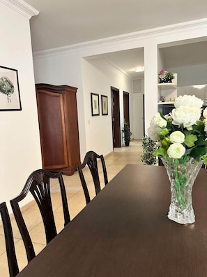 A dining area with a long table, chairs, a vase with flowers, framed pictures on the wall, and a wooden cabinet. - Fort Cambridge - Sliema - Malta (Sliema)