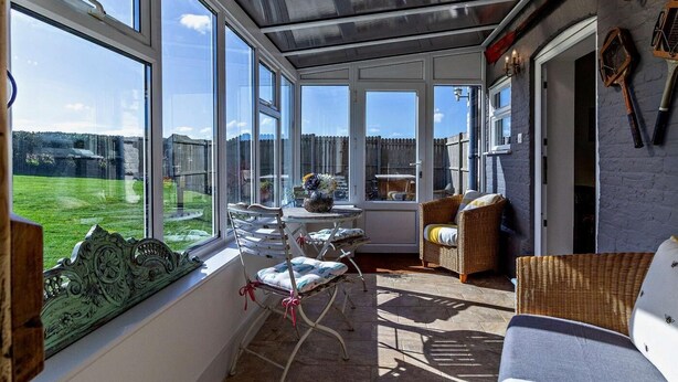 Un solárium con ventanas amplias, mobiliario de mimbre y vistas a un jardín trasero cercado.