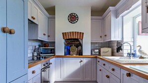 Una cocina con armarios blancos, encimera de madera, un reloj en la pared y una figurita de pato.
