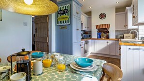 Una cocina con una mesa lista para el desayuno, una cafetera y un reloj en la pared.