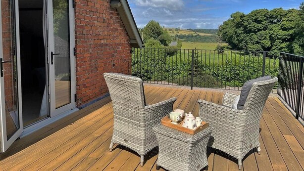 A deck with wicker furniture and a tray of teapots, overlooking a rural landscape. - 3 Bed in Presteigne (oc-78350) (Kinsham)