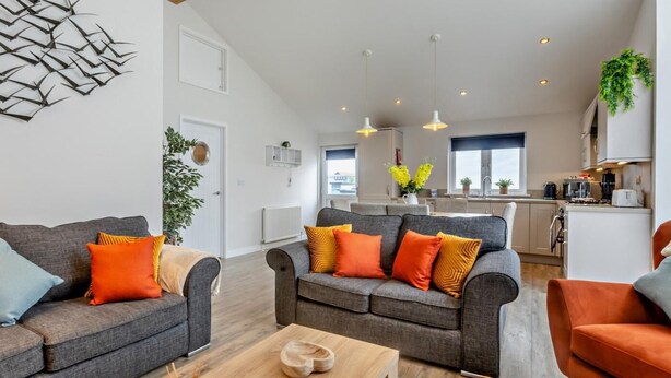 A modern living room with grey sofas, orange cushions, and a wooden coffee table. - 3 Bed in Bideford (oc-64410) (Northam)