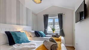 A hotel room with two beds, a window with curtains, a flat-screen TV, and a ceiling light fixture. - 3 Bed in Bideford (oc-64410) (Northam)