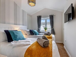 A hotel room with two beds, a window with curtains, a flat-screen TV, and a ceiling light fixture. - 3 Bed in Bideford (oc-64410) (Northam)