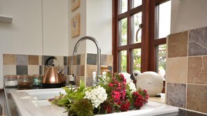 Una cocina con un lavamanos blanco, hervidor de cobre y flores decorativas.