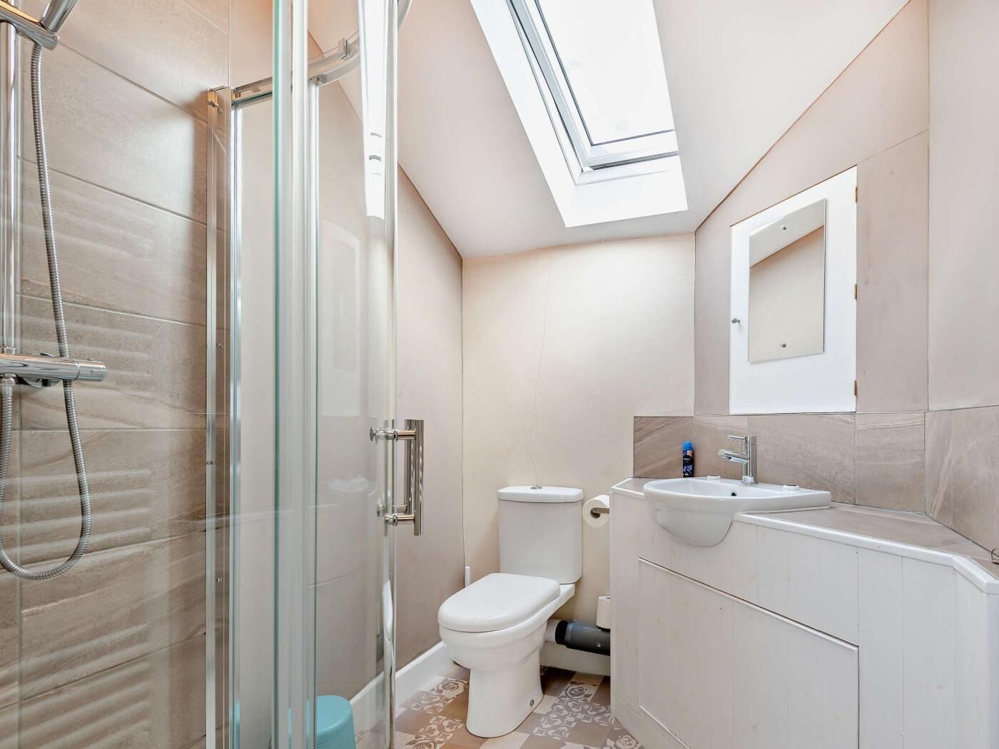 A bathroom with a glass-enclosed shower, a toilet, a sink, and a skylight.