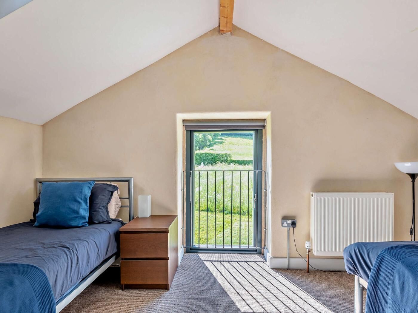 A bedroom with a bed, a nightstand, a dresser, a radiator, and a view of a green landscape through a door.