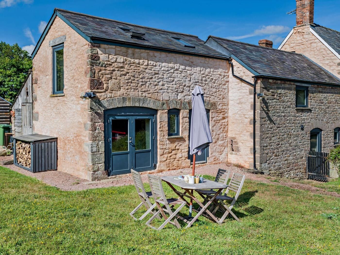 A stone building with a dark door, a small window, and a table with chairs outside.