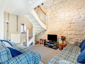 Ein Wohnzimmer mit Steinwand, einer Treppe, einem Flachbildfernseher und karierten Sofas.