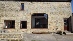Ein Steinhaus mit einem großen Rundbogenfenster, einem kleineren Fenster und einer Tür.
