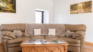 Ein sandfarbenes Ledersofa mit Decke, drei Kissen und einem Couchtisch aus Holz mit geschnitzten Verzierungen.