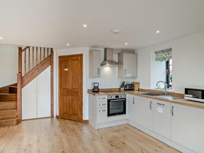 Eine moderne Küche mit Holzboden, weißen Schränken, einem eingebauten Backofen und einer Holztreppe.