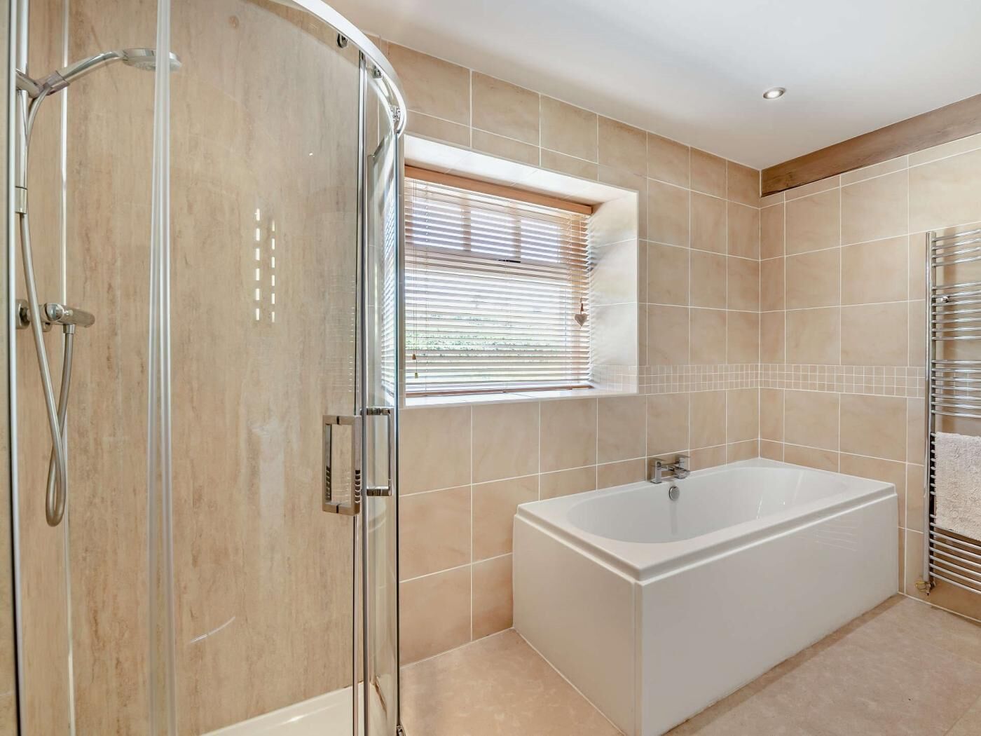 A modern bathroom with a glass shower enclosure, a window with blinds, a white bathtub, and a towel rack.