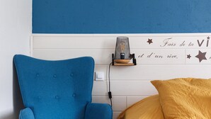 Un fauteuil bleu, un lit avec une couverture jaune et une lampe fixée au mur.