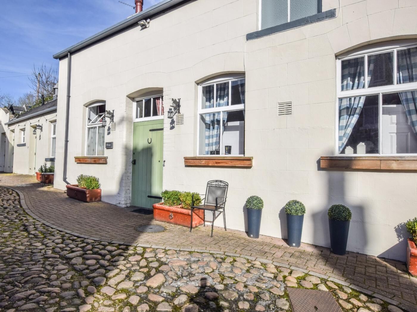 A white building with a green door, potted plants, and a chair outside.