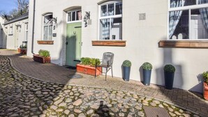 Ein weißes Gebäude mit grüner Tür, Topfpflanzen und einem Stuhl vor der Fassade.