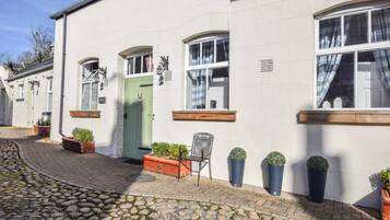 A white building with a green door, potted plants, and a chair outside.
