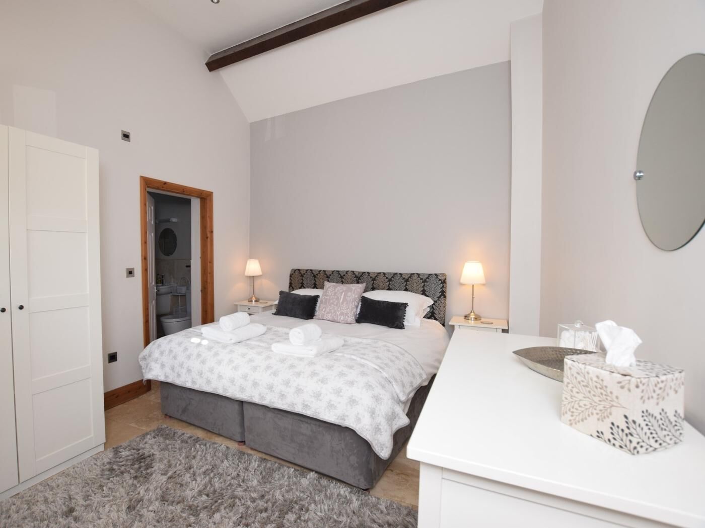 A bedroom with a bed, bedside lamps, a bedside table with a tissue box, and a mirror on the wall.