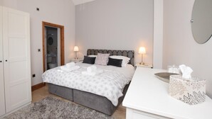 Ein Schlafzimmer mit einem Bett, Nachttischlampen, einem Nachttisch mit Taschentuchbox und einem Spiegel an der Wand.