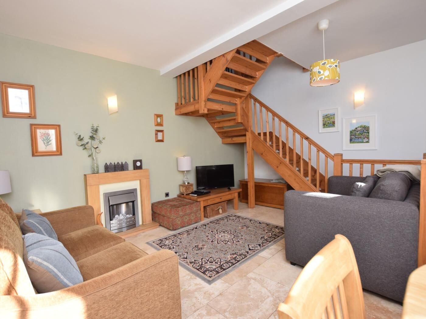 A living room with a fireplace, sofa, TV, and a wooden staircase.