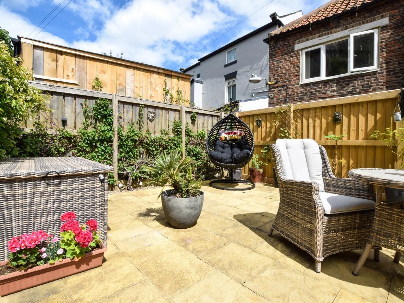 A patio with wicker furniture, a hanging chair, and potted plants.