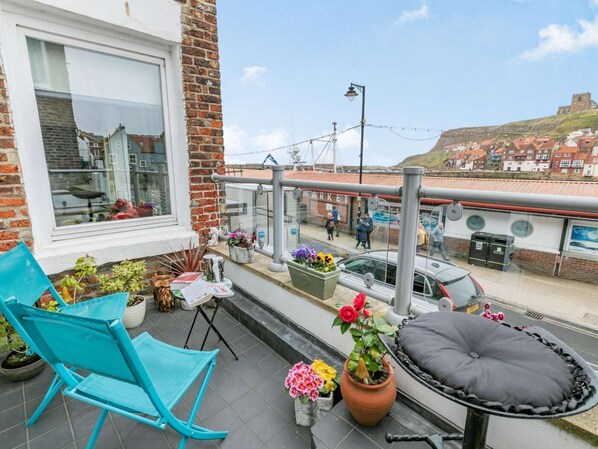 Un balcon avec une chaise, des plantes en pot, un coussin et une vue sur un marché et des immeubles.