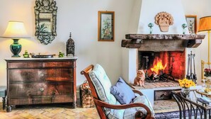 A cozy living room with a fireplace, a wooden cabinet, a chair with cushions, and a lamp. - Villa Giulia (Campania)